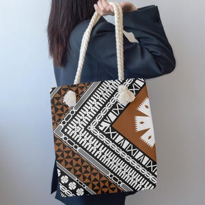 Könnte beinhalten: Eine Tragetasche mit einem geometrischen Muster in Schwarz, Weiß und Braun. Die Tasche hat weiße Seilgriffe und Quasten. Das Design umfasst Dreiecke, Linien und blütenartige Formen.