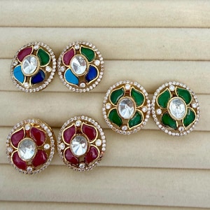 May include: Three pairs of circular stud earrings featuring a central clear stone surrounded by four coloured petal-shaped stones and a border of small clear crystals. One pair has multicoloured petals, one has green petals, and one has red petals.