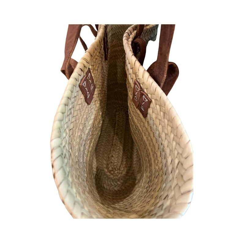 May include: Woven straw tote bag with brown leather handles and accents. The bag has a natural color with a woven pattern and a spacious interior. The handles are attached with brown leather patches.
