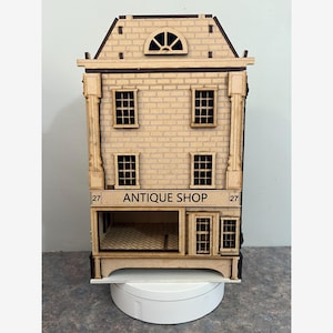 May include: A miniature wooden antique shop model with a brick facade, multiple windows, and a sign that reads "ANTIQUE SHOP". The model has a detailed design, including a decorative roof and columns. The number "27" is on either side of the sign.