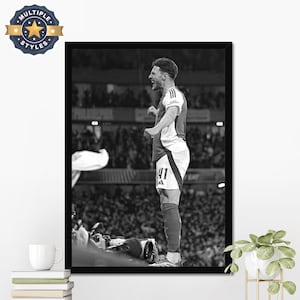 May include: Black and white framed print featuring a soccer player in a jersey with the number 41, celebrating a goal. The image captures the player's emotion and the energy of the crowd in the background. The print is displayed on a white wall.