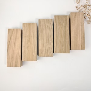 May include: Five rectangular wooden blocks in a stepped arrangement. The blocks are made of light-coloured wood, displaying a natural grain pattern. The blocks vary in height, creating a visual step-like effect. The wood has a warm, neutral tone.