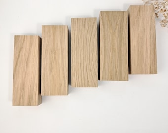 May include: Five rectangular wooden blocks arranged in a staggered pattern. The blocks are made of light-colored wood, showcasing a natural grain. The blocks are of varying heights, creating a visual step-like effect. The wood has a warm, neutral tone.