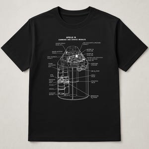 May include: Black t-shirt featuring a detailed white schematic of the Apollo 14 Command and Service Modules. The diagram includes labels for various components like the heater display, battery, and oxygen tanks, offering a technical illustration.