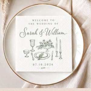 May include: A white square paper napkin featuring dark green printed text that reads WELCOME TO THE WEDDING OF Sarah & William 07.10.2026. The design includes a line art illustration of a table setting with a plate, cutlery, glasses, and candles.
