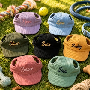 May include: Seven corduroy pet hats in purple, blue, olive green, black, yellow, pink, and sage green. Each hat features ear holes and embroidered names: Pippa, Luna, Oliver, Bear, Buddy, Roscoe, and Finn in contrasting thread colours.