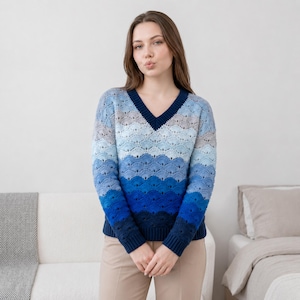 May include: A blue V-neck sweater with a wave-like pattern. The sweater transitions from light blue at the top to a deep navy blue at the bottom. The sleeves and neckline are a solid navy blue.