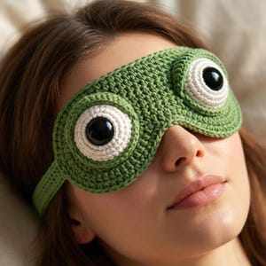 Puede incluir: Una máscara para dormir verde tejida a ganchillo con grandes formas de ojos redondos. La máscara presenta detalles blancos y negros para imitar los ojos. La máscara para dormir está diseñada para bloquear la luz y promover la relajación. La máscara está hecha de hilo suave.