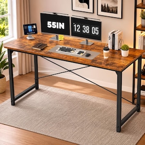 May include: A rectangular desk with a rustic brown wood-grain surface and a black metal frame featuring X-shaped crossbars. The desk holds two computer monitors, one displaying 55IN, a keyboard, a mouse, a tablet, a notebook, and a cup.