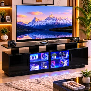 May include: A black media console with a flat top surface, two solid side cabinets, and two central glass-front cabinets illuminated by blue interior LED lighting. The console holds a large flat-screen television displaying a mountain landscape.