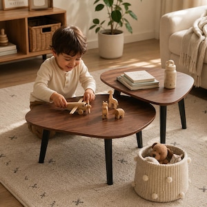 May include: Two dark brown, kidney-shaped coffee tables with black legs. A child plays with wooden toys, including a plane, giraffe, and hippo, on one table. A woven basket with a teddy bear and other toys sits nearby. The scene is set on a patterned rug.