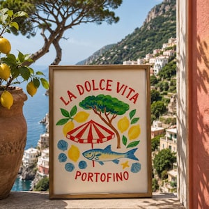 以下が含まれることがあります： LA DOLCE VITAとPORTOFINOの文字が入ったカラフルなイラストの長方形の額入りプリント。赤と白のストライプのビーチパラソル、緑の木、黄色のレモン、青い魚、青い貝殻が描かれています。