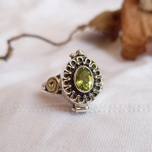 May include: Silver ring featuring an oval, light green gemstone. The ring has an ornate, detailed setting with a floral design around the gemstone. The ring's band has a spiral design on the sides.