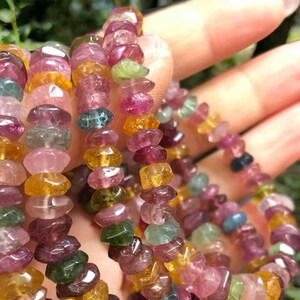 May include: A collection of colorful tourmaline gemstone bracelets. The beads are a mix of pink, green, yellow, and blue hues. The bracelets are strung together, showcasing the natural, irregular shapes of the stones.