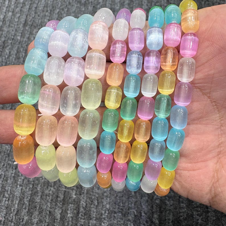 May include: A collection of colorful, oval-shaped beads in shades of blue, pink, yellow, and green. The beads are strung together, creating a bracelet-like appearance. The beads are held in a hand, showcasing their various pastel hues.