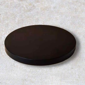 K&ouml;nnte beinhalten: Ein massives, dunkelbraunes, kreisf&ouml;rmiges Objekt mit flacher Oberseite und leicht abgerundeter Kante. Das Objekt ist vor einem neutralen, strukturierten Hintergrund platziert, was auf ein minimalistisches Design hindeutet.