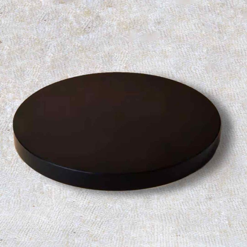 K&ouml;nnte beinhalten: Ein massives, dunkelbraunes, kreisf&ouml;rmiges Objekt mit flacher Oberseite und leicht abgerundeter Kante. Das Objekt ist vor einem neutralen, strukturierten Hintergrund platziert, was auf ein minimalistisches Design hindeutet.