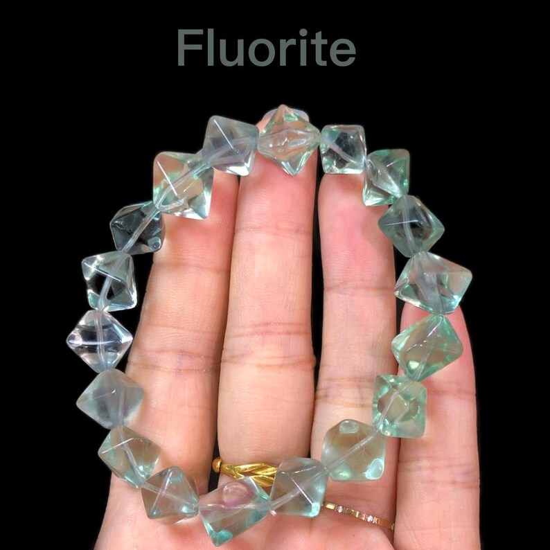 May include: A bracelet made of faceted, translucent fluorite beads in shades of green and clear. The beads are square-shaped and strung together. The word "Fluorite" is displayed in white text at the top of the image.