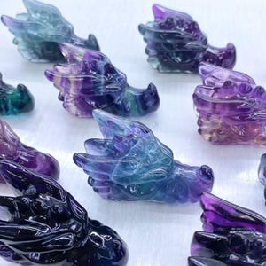 May include: A selection of carved dragon heads in shades of purple, blue, and green. The dragon heads are made of a translucent material, with visible carving details. The dragons are arranged in a grid pattern.