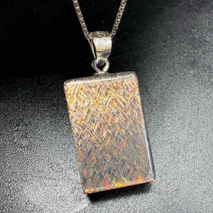 May include: A rectangular pendant with a silver chain. The pendant has a shimmering, multi-colored surface with gold, brown, and iridescent hues. The pendant is approximately 1 inch long.