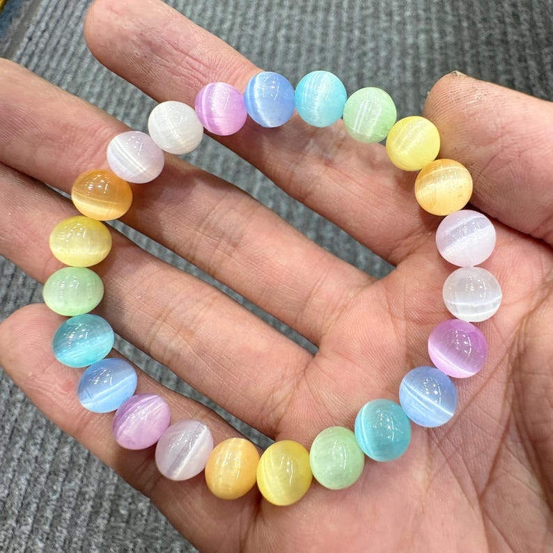 May include: A colorful beaded bracelet featuring a rainbow of pastel-colored, round beads. The beads are in shades of pink, blue, green, yellow, and orange. The bracelet is held in a hand.