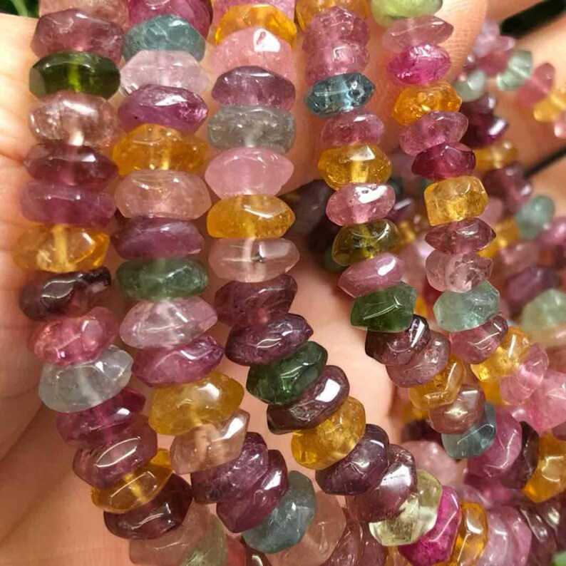 May include: Strands of colorful tourmaline beads in shades of pink, green, yellow, and purple. The gemstones are irregularly shaped and strung together, creating a vibrant and natural look. The beads are likely used for jewelry making.