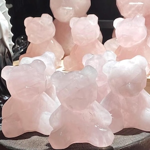May include: A collection of rose quartz bear figurines in various sizes. The bears are a soft pink color and have a smooth, polished finish. The figurines are arranged together, showcasing their carved details.