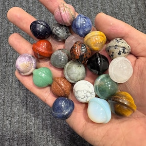 May include: A selection of polished gemstone spheres in diverse colours, such as pink, blue, green, and brown. The spheres are held in a hand, highlighting their smooth surfaces and unique patterns. The gemstones appear to be about 2.5 cm in diameter.