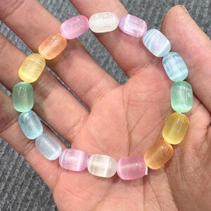 May include: A colorful bracelet composed of smooth, oval-shaped beads in a spectrum of pastel colors, including pink, yellow, green, and blue. The beads are strung together, creating a vibrant and eye-catching accessory. The bracelet is shown on a person's hand.