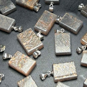 May include: A collection of rectangular pendants with a silver bail. The pendants have a unique, textured pattern in shades of gray, brown, and silver. The pendants are scattered across a dark surface, creating a visually appealing arrangement.