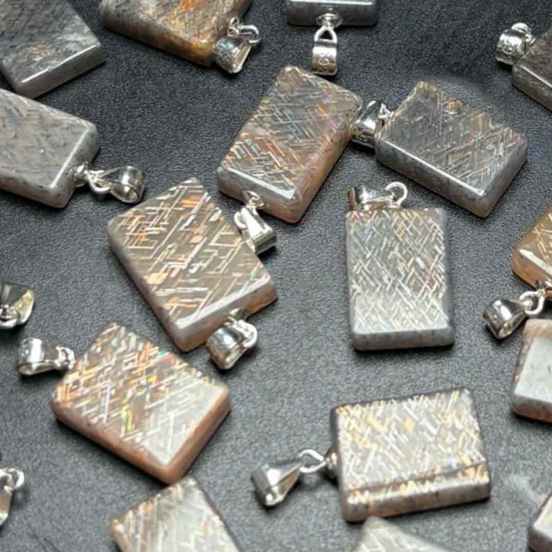 May include: A collection of rectangular pendants with a silver bail. The pendants have a unique, textured pattern in shades of gray, brown, and silver. The pendants are scattered across a dark surface, creating a visually appealing arrangement.