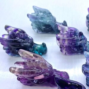 May include: Several small dragon figurines carved from a translucent, multi-coloured stone. The dragons feature shades of purple, blue, and green. They are depicted lying down, with their heads and wings visible. The theme is fantasy and collectibles.