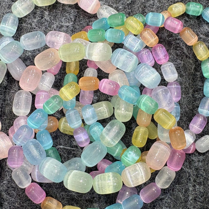 May include: A collection of colorful, translucent gemstone beads in various pastel shades, including pink, blue, green, yellow, and orange. The beads are oval-shaped and strung together, creating a vibrant and eye-catching display. Ideal for jewelry making.
