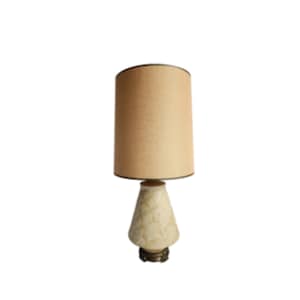 May include: A vintage table lamp with a white ceramic base and a beige fabric lampshade. The base has a textured design and the lampshade has a black trim.