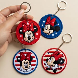 May include: Four round keychains featuring Minnie Mouse. Each keychain has a different design, including red, white, and blue colors. The keychains have a metal ring and chain for attaching to keys or bags. The Minnie Mouse designs include stars and stripes.
