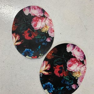 Könnte beinhalten: Zwei runde Stoffuntersetzer mit Blumenmuster. Die Untersetzer haben einen dunklen Hintergrund mit rosa, roten, blauen und gelben Blumen.