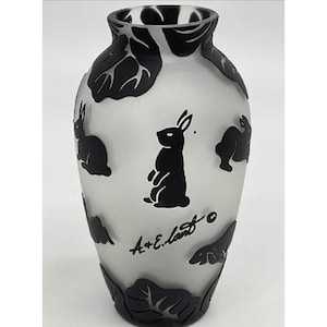 May include: A frosted glass vase with black rabbit silhouettes and leaf designs. The vase features a central standing rabbit and the artist's signature. A decorative piece for home decor.