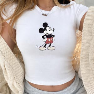 Puede incluir: Top corto blanco de manga corta con un gr&aacute;fico de Mickey Mouse. El personaje de dibujos animados est&aacute; representado en negro, rojo y blanco. El top es acanalado y entallado.