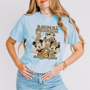 May include: Light blue t-shirt featuring a graphic of Disney characters, including Mickey and Minnie Mouse, Donald Duck, Goofy, and Pluto, with the text "ANIMAL KINGDOM" and "Walt Disney World" in a vintage style.