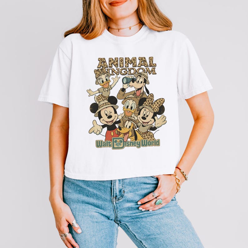 May include: White t-shirt featuring a retro-style graphic of Disney characters, including Mickey and Minnie Mouse, Donald Duck, and Goofy. The design includes the text "ANIMAL KINGDOM" and "Walt Disney World" in a vintage font.