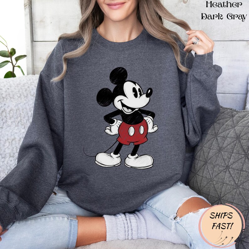 May include: Heather dark gray sweatshirt featuring a classic Mickey Mouse graphic. The cartoon character is depicted in black, white, and red, with his signature shorts and shoes. The sweatshirt has long sleeves and a crew neck.