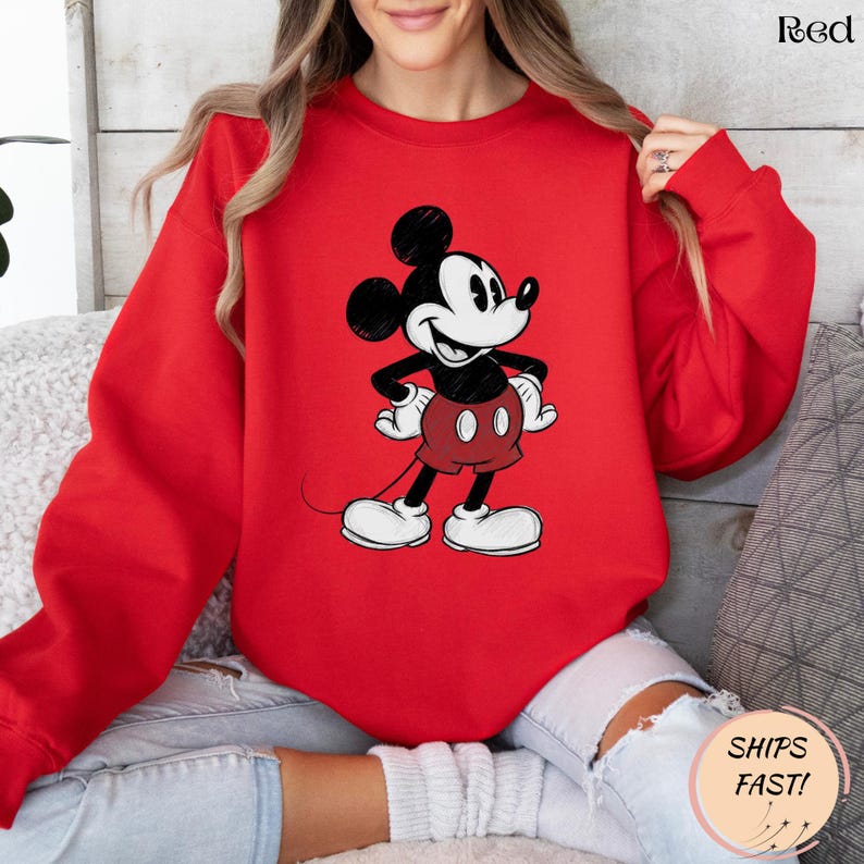 May include: Red sweatshirt featuring a classic Mickey Mouse graphic. The cartoon character is depicted in black, white, and red, with his signature shorts and gloves. The word "Red" is printed in the upper right corner.