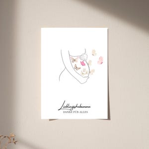 Op de afbeelding: Een witte rechthoekige print met een zwarte lijntekening van een zwangere romp met handen op de buik. Verschillende aquarel-stijl vlinders in roze en beige tinten omringen de buik. De tekst luidt: Lieblingshebamme DANKE FÜR ALLES.