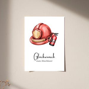 May include: A white greeting card featuring a red firefighter helmet with a gold shield and a red fire extinguisher illustration. Below the graphics, the black text reads "Glückwunsch zum Abschluss!" in a combination of script and serif fonts.