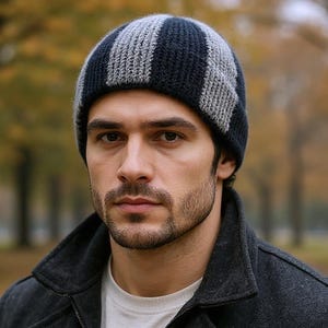 May include: A navy blue and grey striped knitted beanie hat. The person is wearing a dark grey coat and a white shirt. The background is a blurred view of a park with trees.
