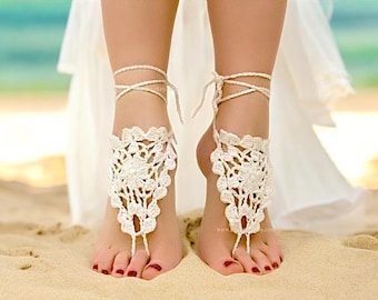 May include: White crocheted barefoot sandals with a floral design. The sandals are tied around the ankles with white cords.