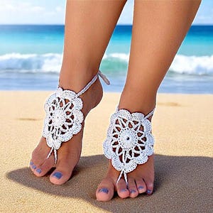 May include: White crochet barefoot sandals with a floral design. The sandals are worn on a woman's feet on a sandy beach.