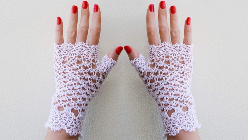 May include: A pair of white crocheted fingerless gloves with a delicate floral pattern. The gloves are made with a fine yarn and have a lacy look.