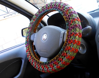 May include: A colorful crocheted steering wheel cover in shades of red, green, purple, and brown. The cover is made of a thick yarn and has a textured pattern.