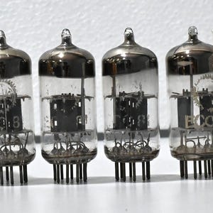 Può includere: Quattro tubi a vuoto Valvo ECC81 con involucri in vetro trasparente e componenti metallici interni, disposti in fila. Ogni tubo è accompagnato da una scatola di cartone bianco con specifiche tecniche stampate e il testo Valvo ECC81.